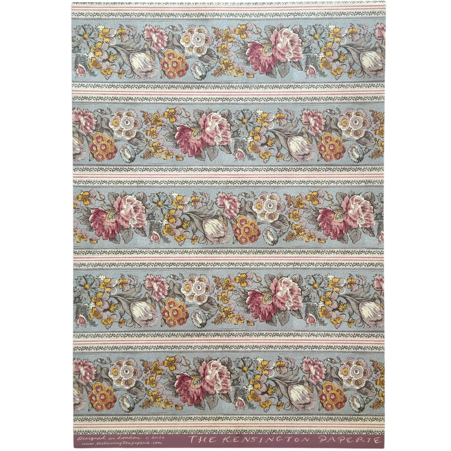 A floral patterned wrapping paper with large flowers in pink, cream, yellow, and muted green on a pale blue-gray background, divided by narrow decorative borders.