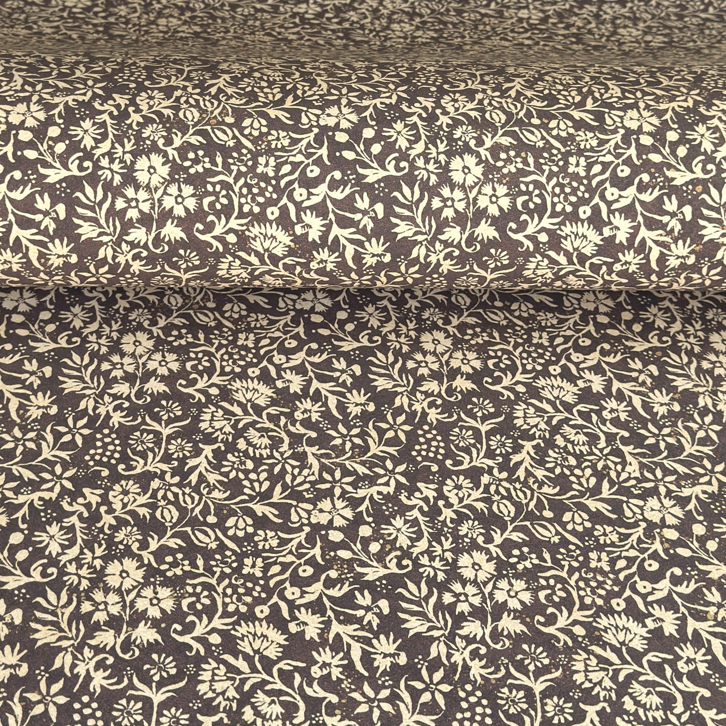 A sheet of dark aubergine wrapping paper with a dense cream floral and vine pattern