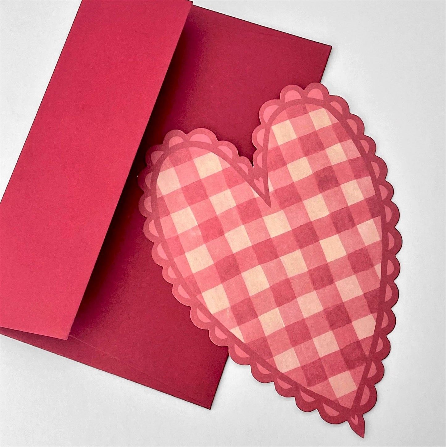 A heart shaped postcard with a red and pink gingham pattern. By Wanderlust, pictured with red envelope