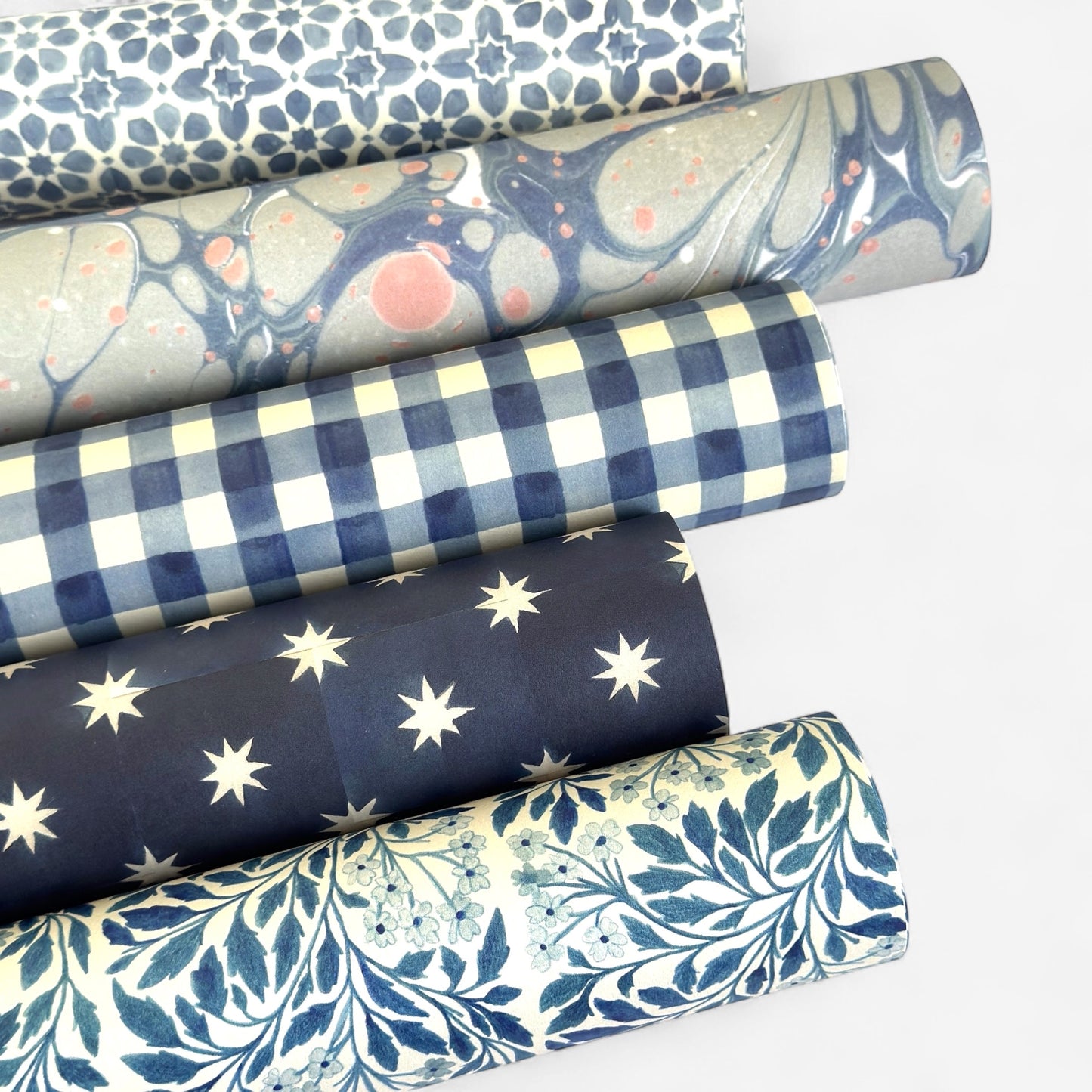 blue and white gingham patterned wrapping paper by Wanderlust. Pictured rolled with other patterned papers