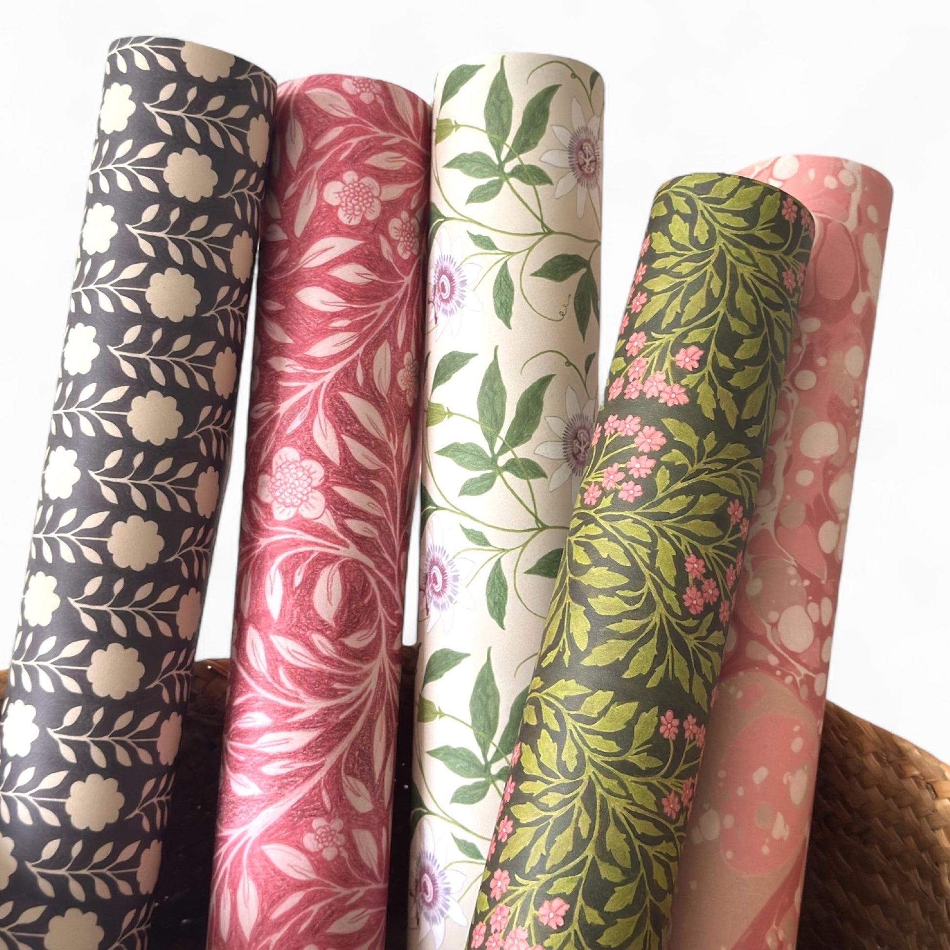 floral wrapping paper with pink passion flowers, green leaves on a cream background . Pictured rolled with other designs