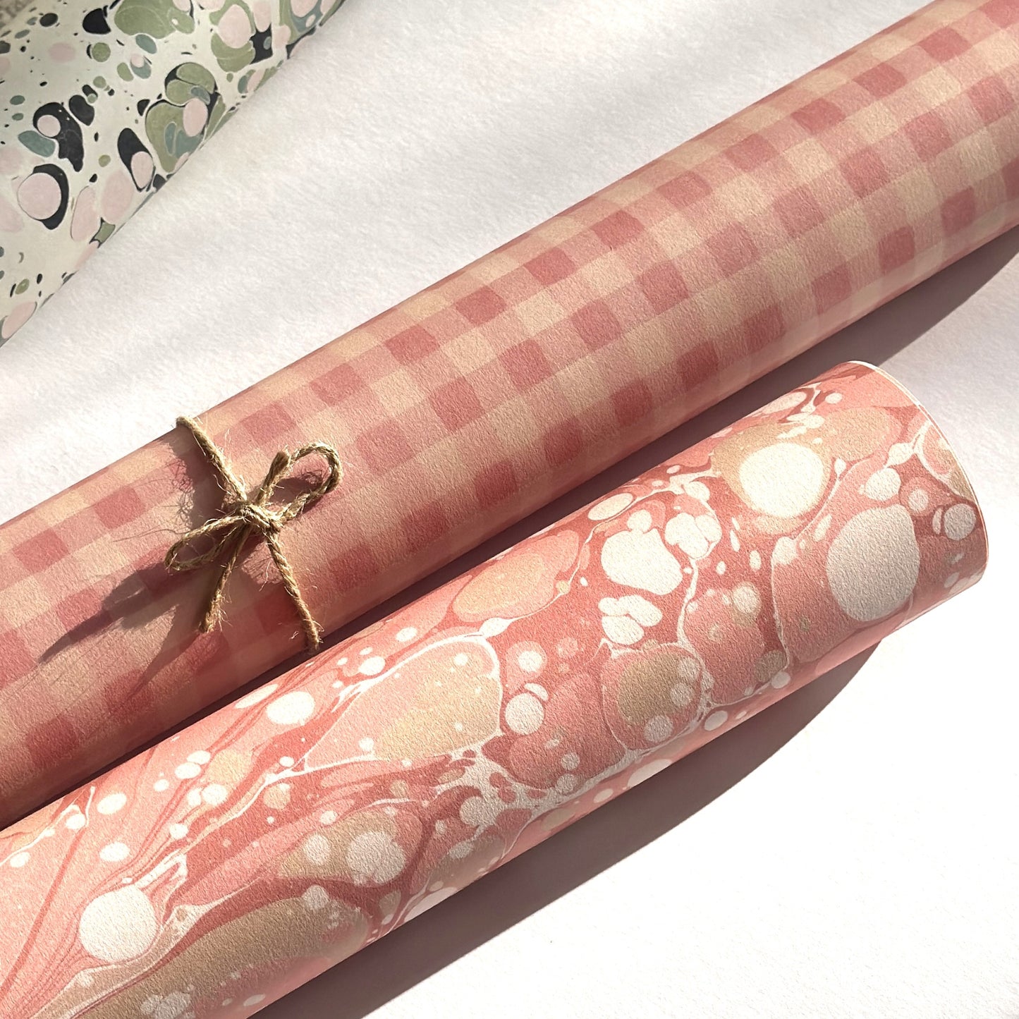 Checkered pattern wrapping paper with pink and beige squares. Pictured rolled alongside a roll of pink marbled paper
