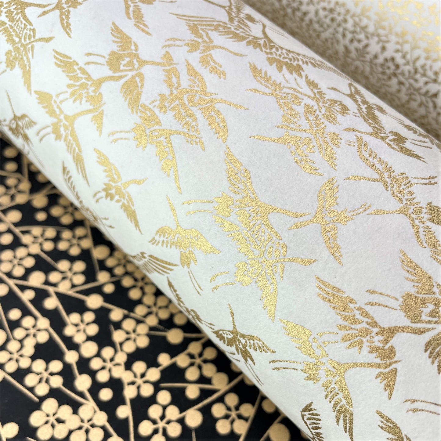 japanese silk-screen handmade paper showing gold cranes in flight on ivory backdrop, lifestyle shot with other papers