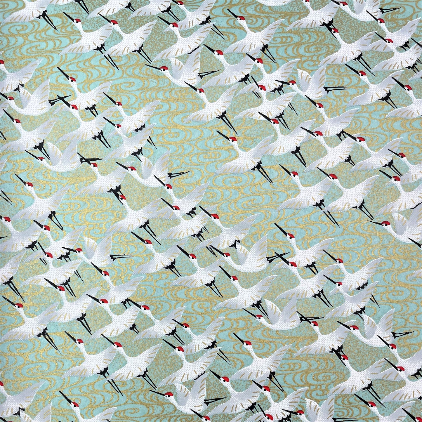 japanese silk-screen handmade paper showing white cranes in flight on a light teal and gold backdrop