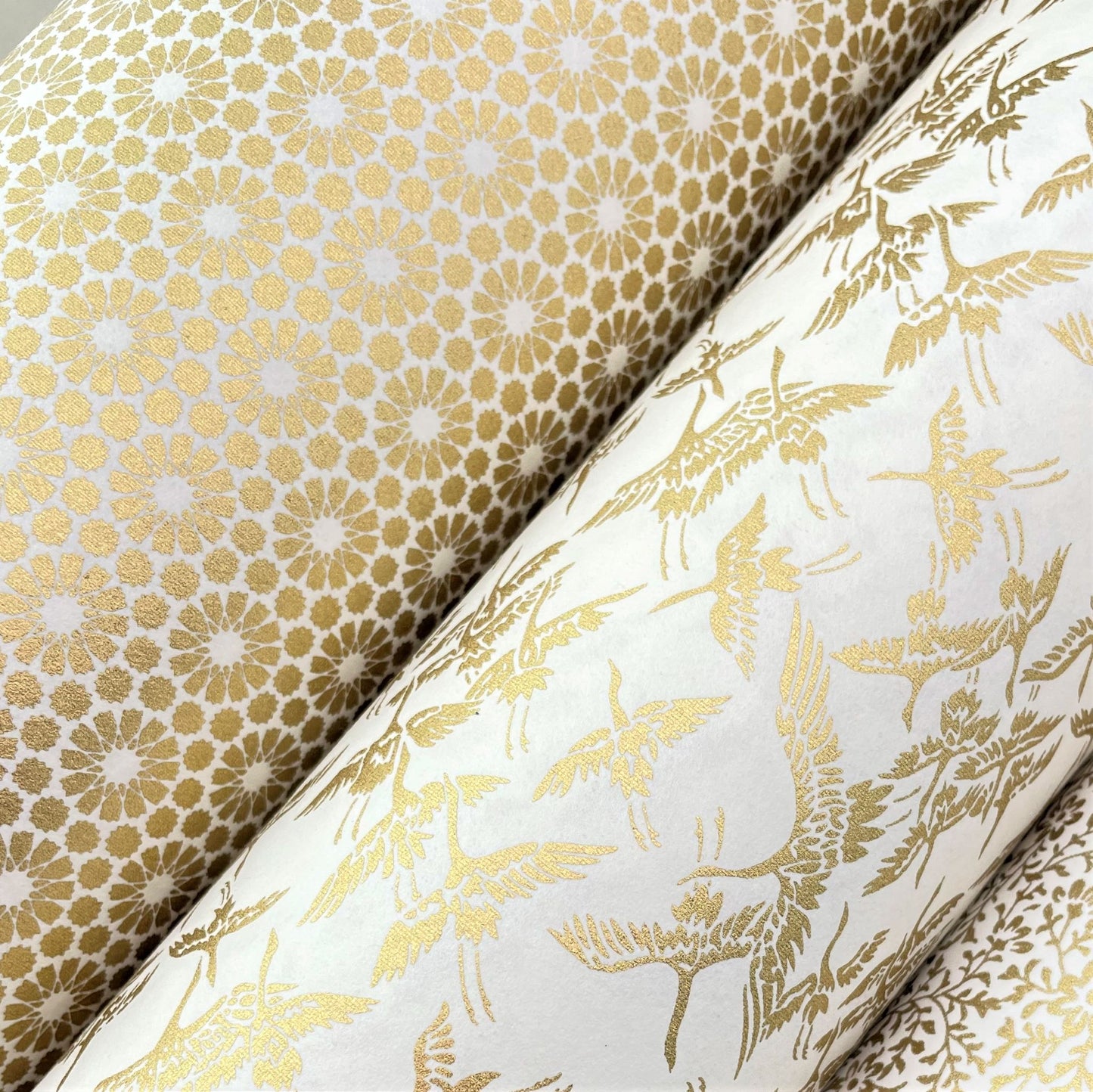 japanese silk-screen handmade paper showing gold repeat chrysanthemum flower motif repeat, lifestyle shot with other gold papers