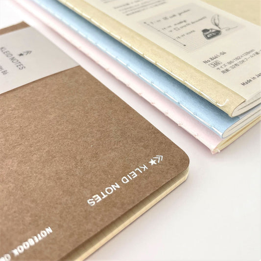 Soft cover notebook with grid format pages. Cover is plain brown with branded belly band, close-up