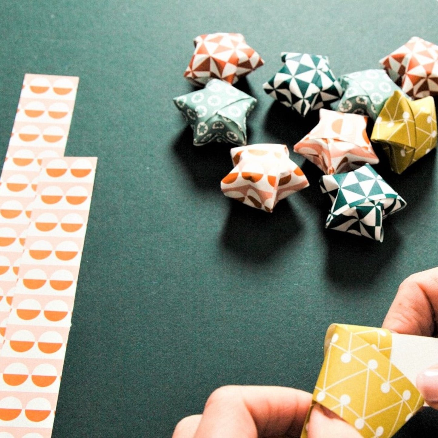 A garland of small paper origami patterned stars "lucky stars" in mustard, teal, aqua and orange, close-up of how the stars are made
