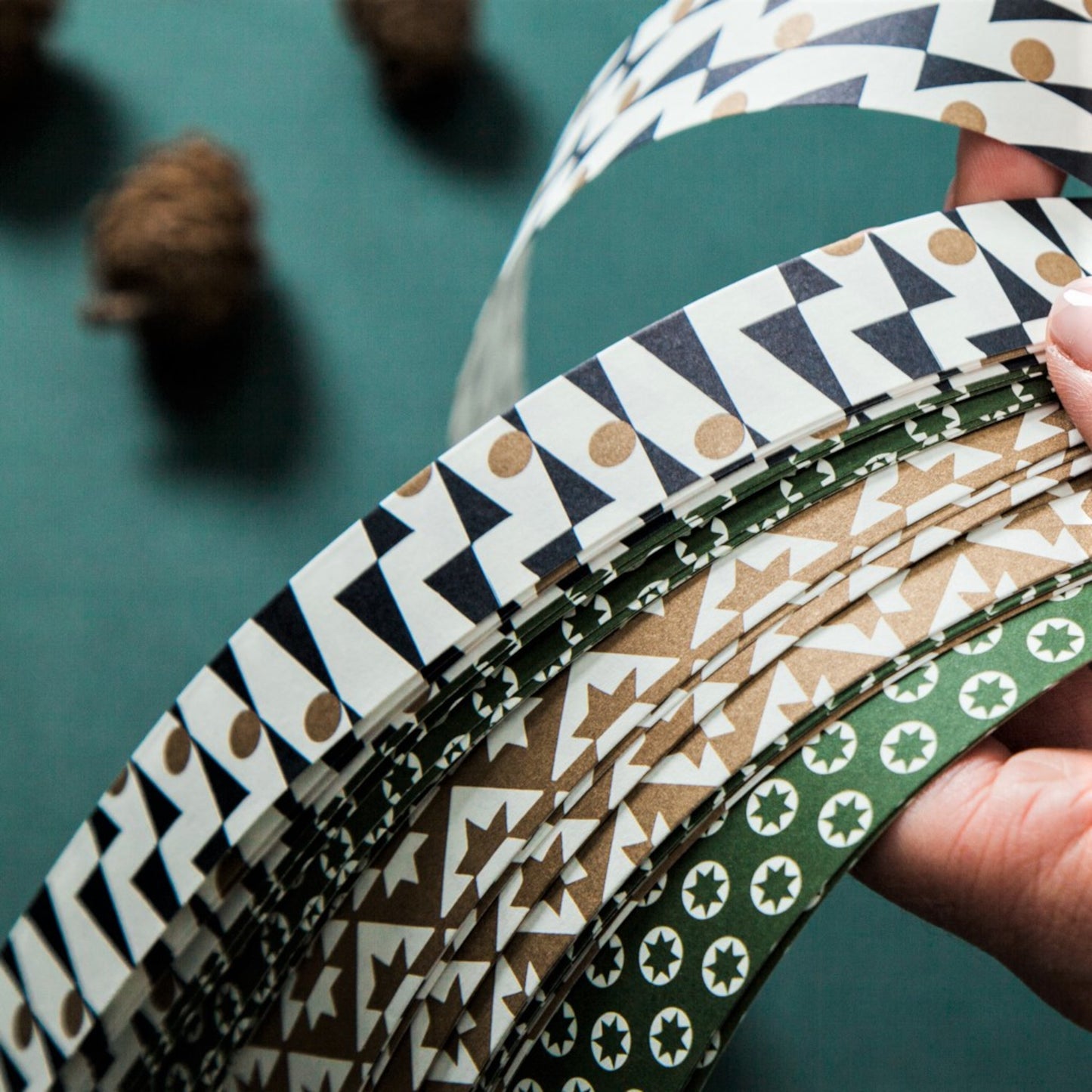 A garland of small paper origami patterned stars "lucky stars"  pictured are the patterned paper strips used to make the starsin green, gold and dark blue