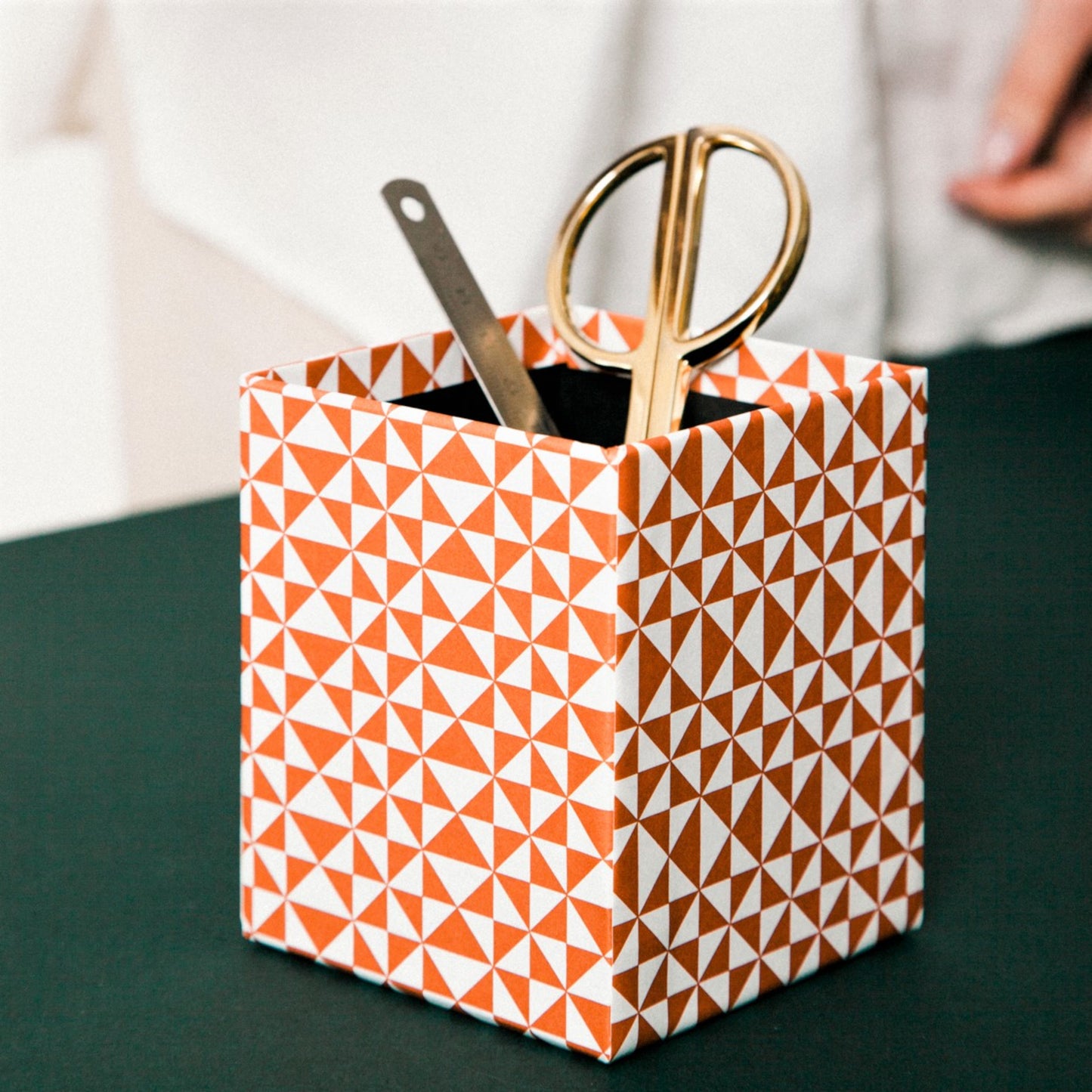 Square pencil pot covered in geometric triangular brick red and white patterned paper, lifestyle shot