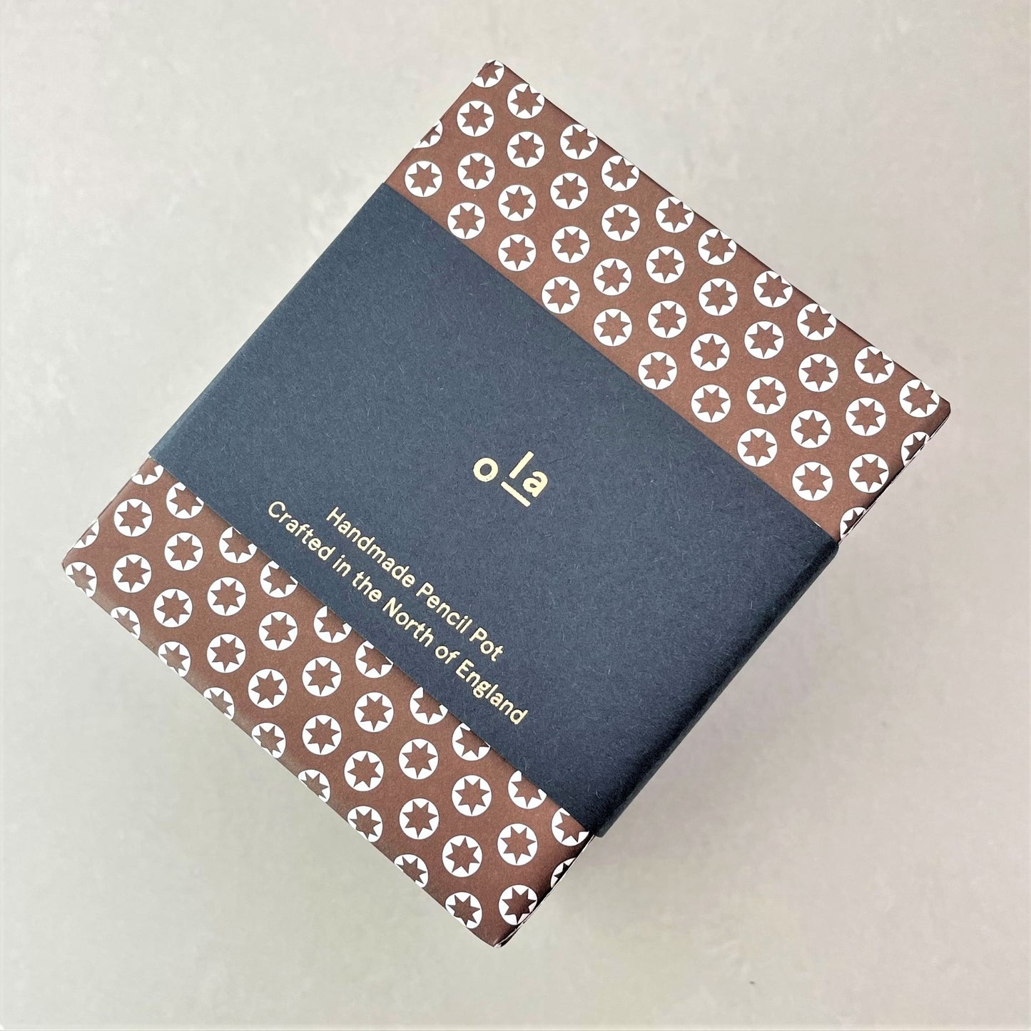 Square pencil pot covered in brown patterned paper with a repeat pattern of tiny white stars, pictured with branded belly band