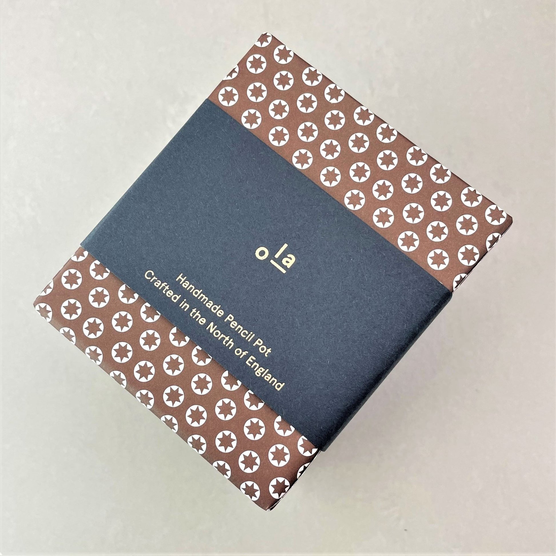 Square pencil pot covered in brown patterned paper with a repeat pattern of tiny white stars, pictured with branded belly band