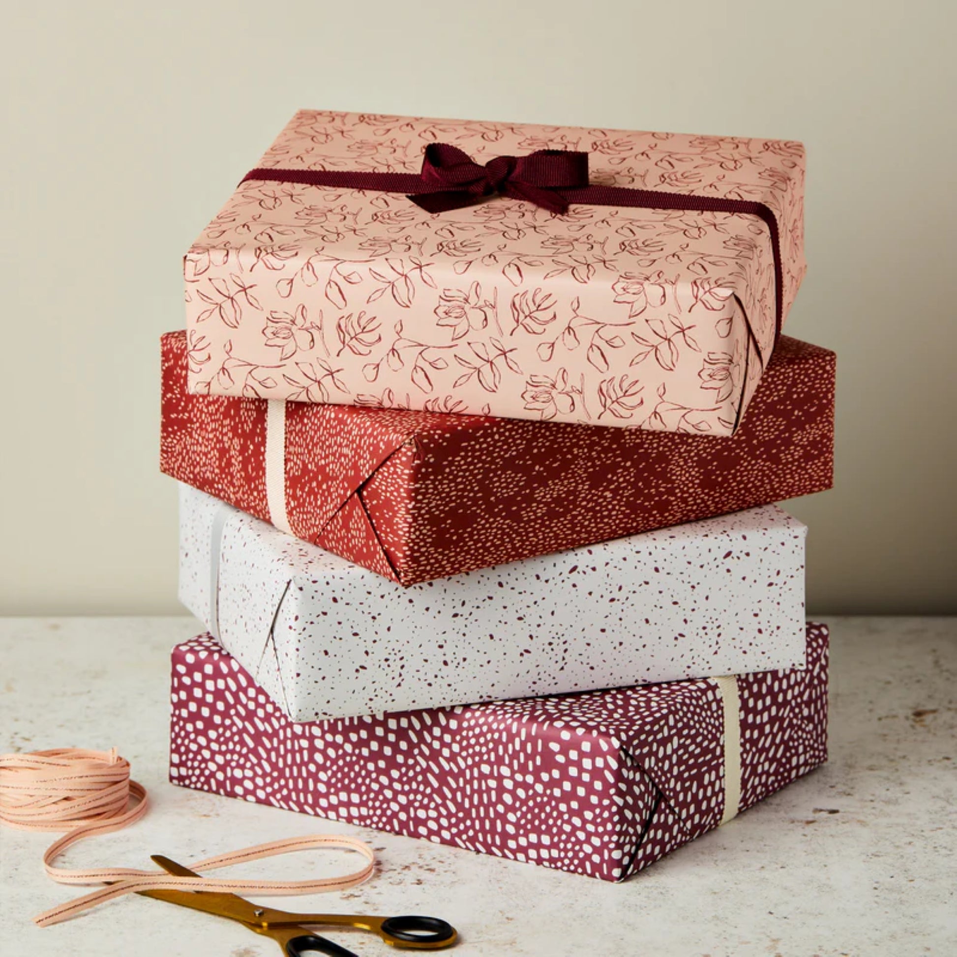 Four wrapped presents in abstract paper patterns in colours of blush pink, rust, white and aubergine by Ink & Bloom