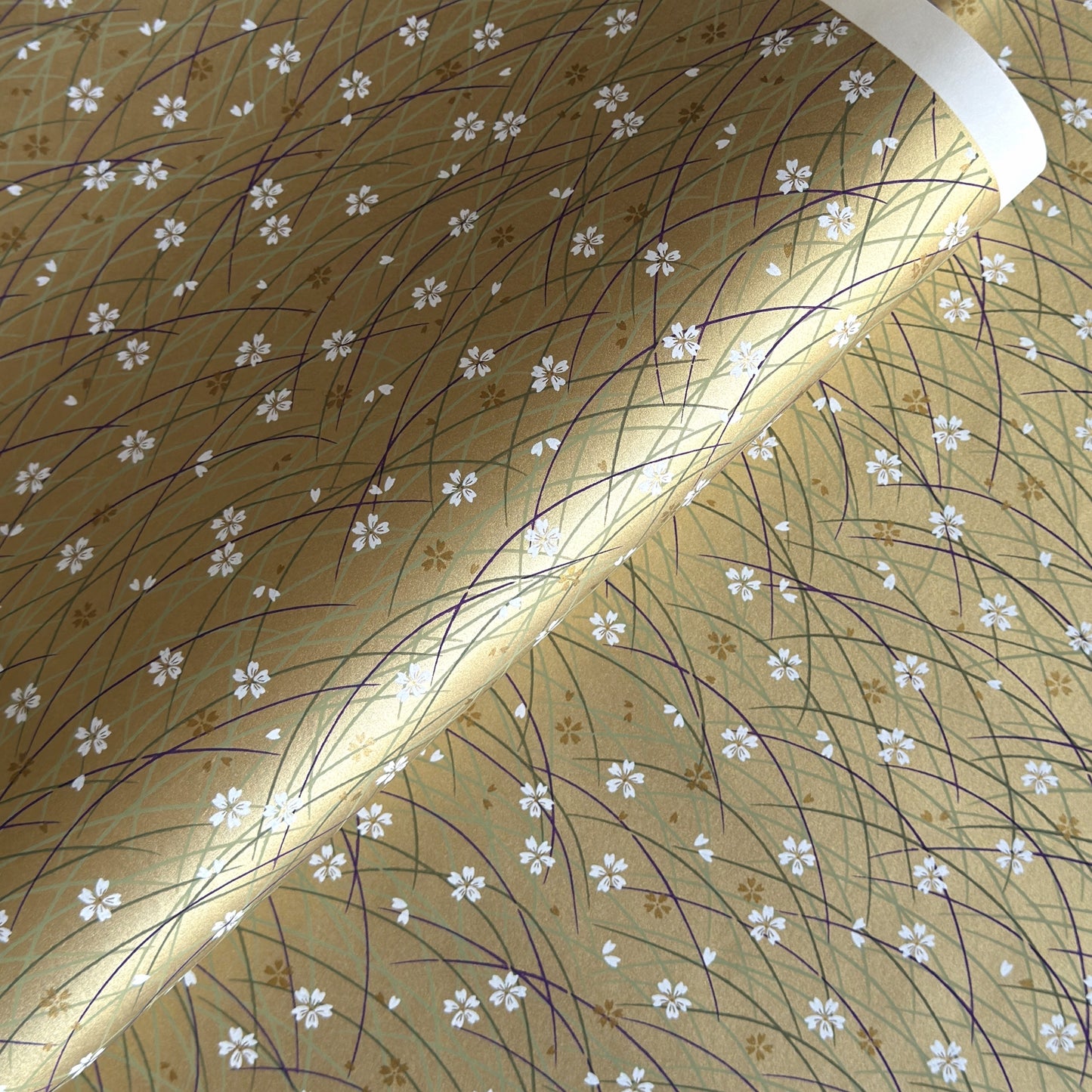 Japanese silkscreen chiyogami paper with a pattern of purple arches and white cherry blossom on antique gold backdrop