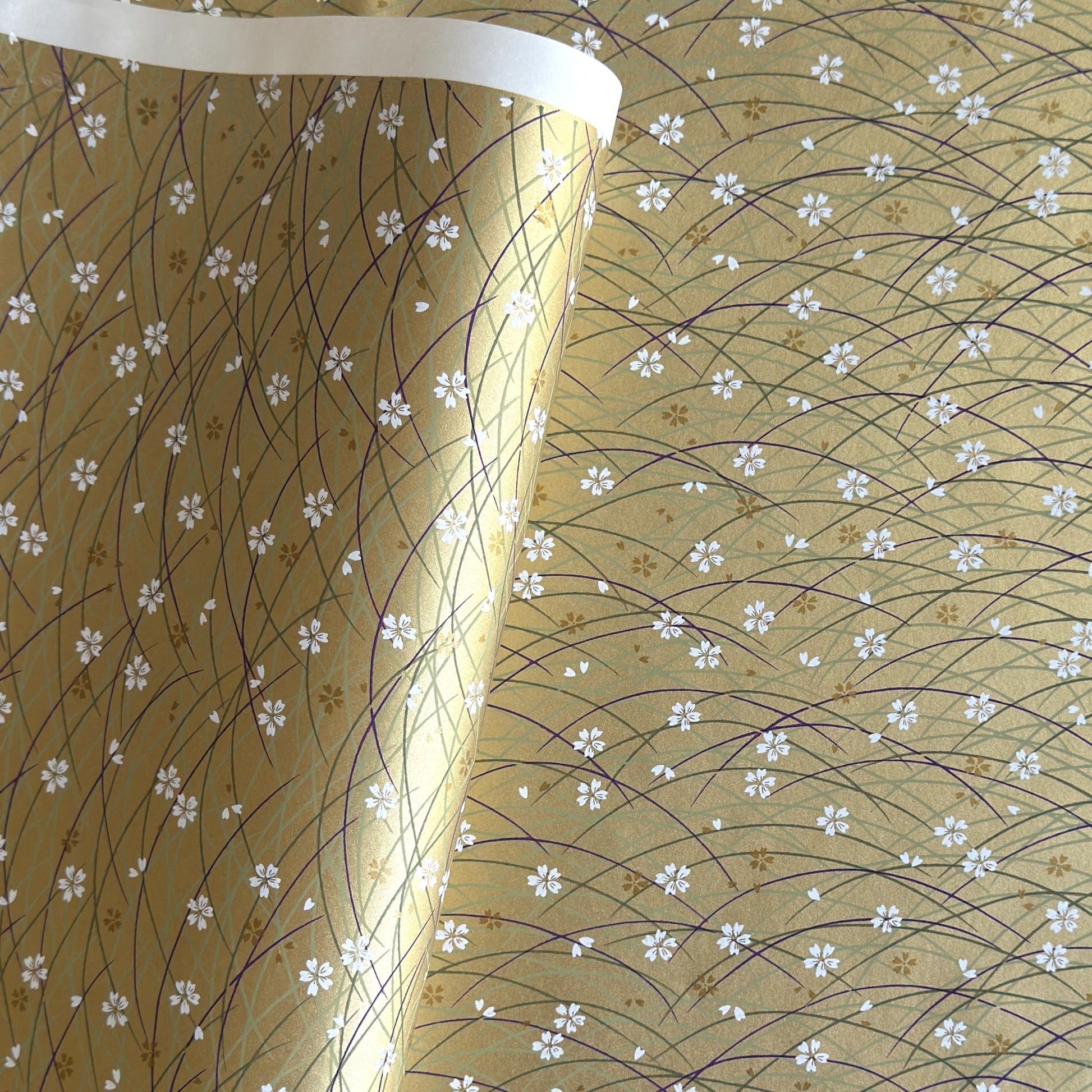 Japanese silkscreen chiyogami paper with a pattern of purple arches and white cherry blossom on antique gold backdrop