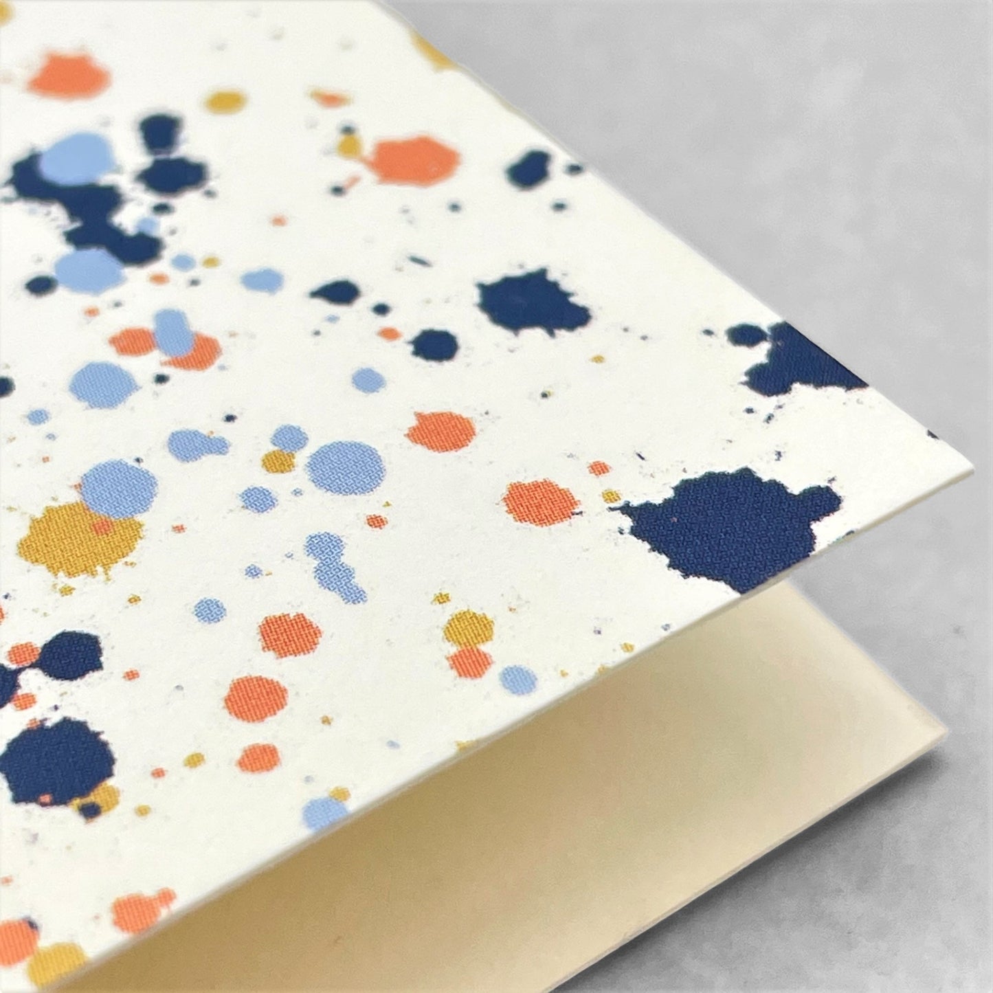 Greetings card with splatter of paint design in navy, pale blue, orange and mustard on ivory paper by amaretti design