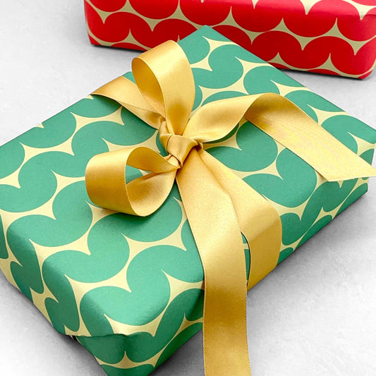 wrapping paper by Anne Davison Studio. Bold green wiggle lines with a retro vibe on beige backdrop.  Pictured as a present with a big gold ribbon