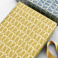 wrapping paper by Anne Davison Studio. Creamy domino outlined shapes on a mustard background. Wrapped as a present
