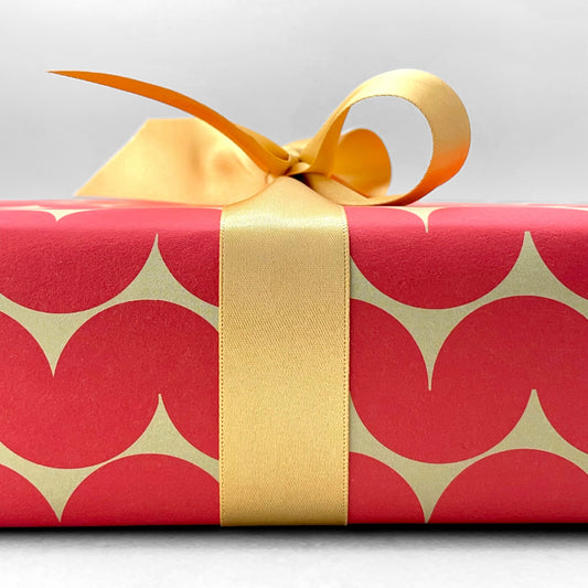 wrapping paper by Anne Davison Studio. Bold red wiggle lines with a retro vibe on beige backdrop.  Shown close up with a bow