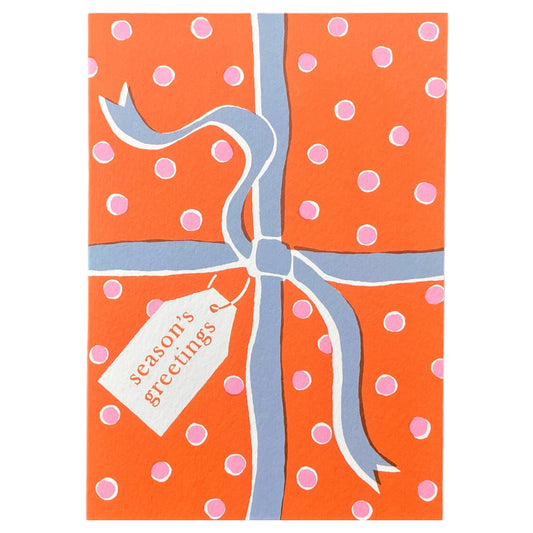 Greetings card with an image of a present wrapped with a bow and a gift tag with "Season's greetings" in orange, pink and blue, by Ariana Martin 