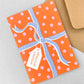 Greetings card with an image of a present wrapped with a bow and a gift tag with "Season's greetings" in orange, pink and blue, by Ariana Martin