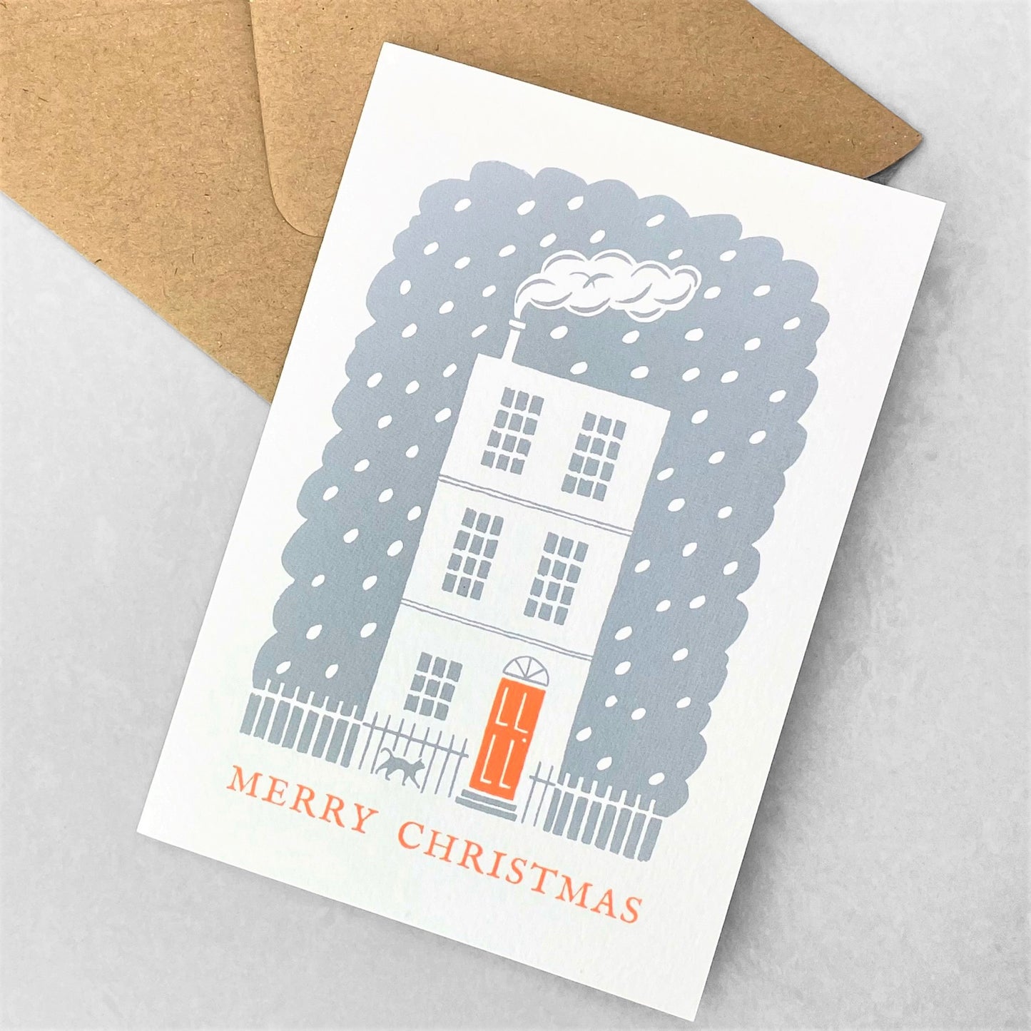 Greetings card of a white house, with an orange door in the snow. Message reads Merry Christmas, by Ariana Martin