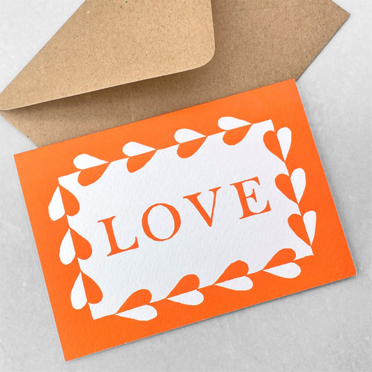 Greetings card with the word LOVE written and a border with hearts in deep orange on a white background. By Ariana Martin