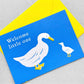 New baby greetings card, with a white duck and duckling on a blue background. words " Welcome little one". Card by Ariana Martin