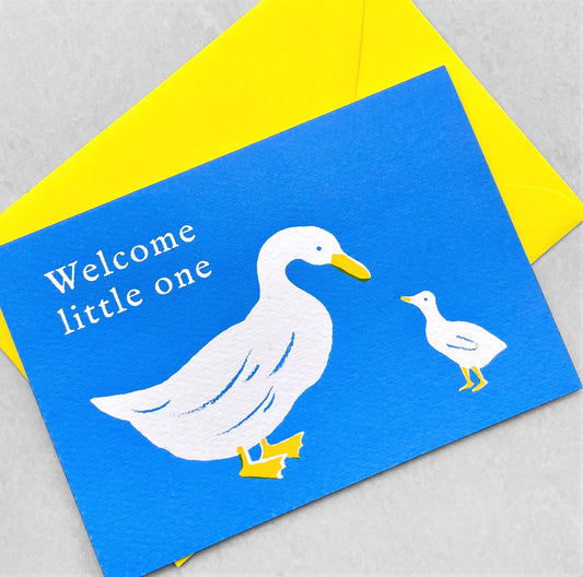 New baby greetings card, with a white duck and duckling on a blue background. words " Welcome little one". Card by Ariana Martin