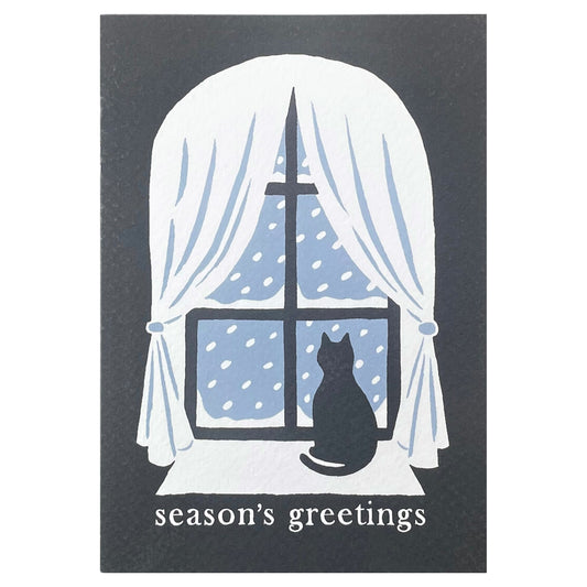 Season's greetings greetings card with a black cat looking out of a window at the snow, by Ariana Martin