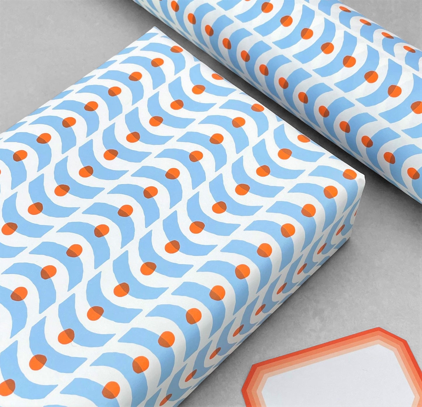 patterned paper, gift wrap with a geometric pale blue wavy pattern and orange dot. By Ariana Martin