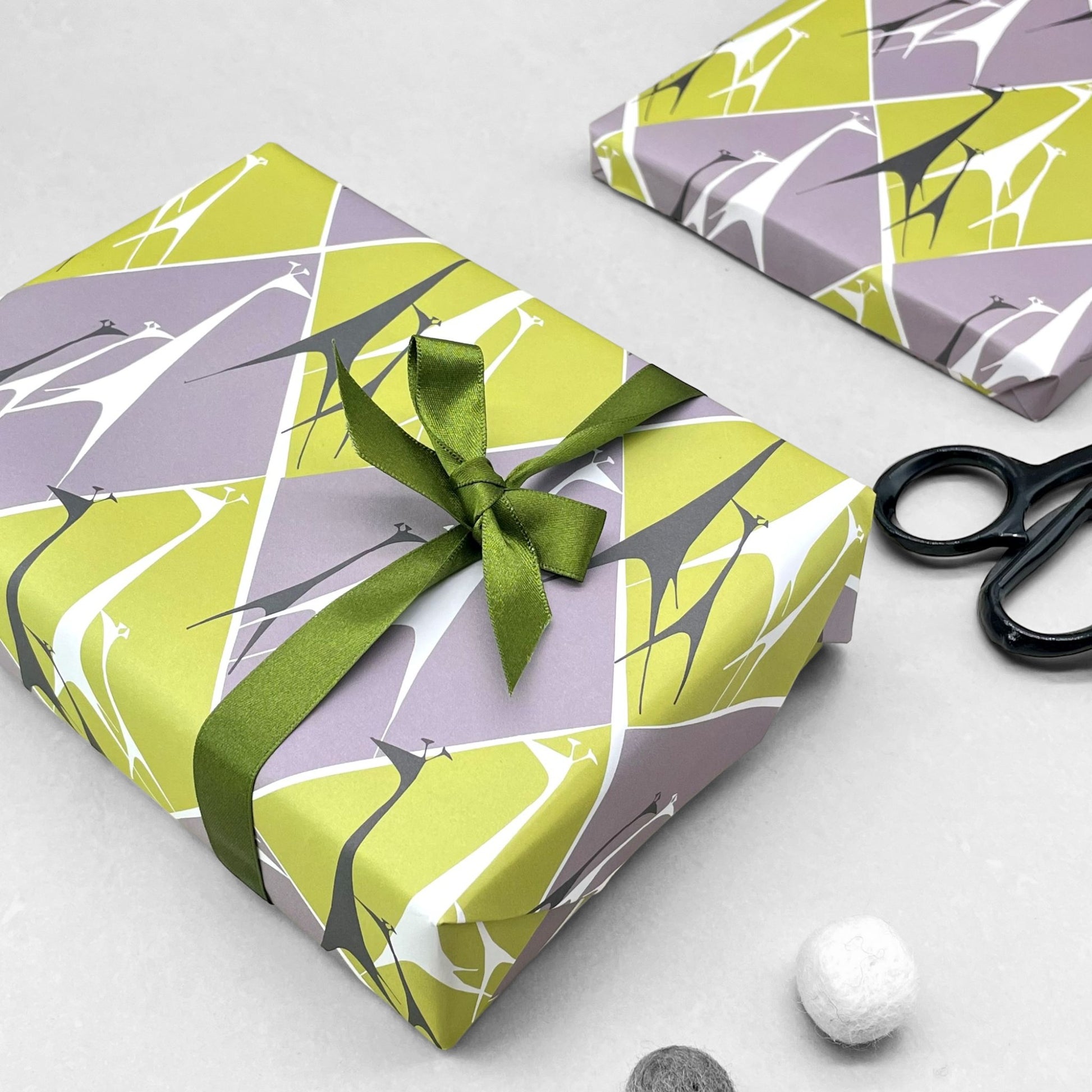 wrapping paper with stylised white and charcoal outline giraffes on a diamond backdrop of green and grey by Artisan Design