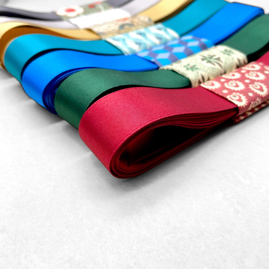 Satin ribbon 25mm wide and 5 metres long, presented with a patterned paper band. colour - scarlet red