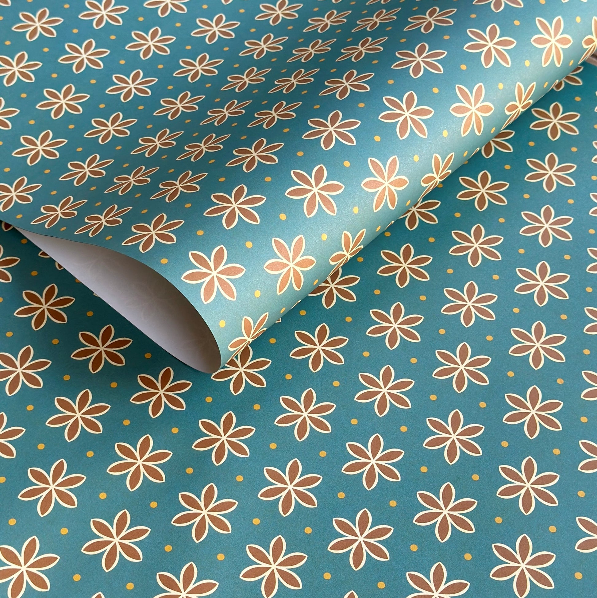 a sheet of wrapping paper with a repeat pattern of stylised brown flowers on a teal green background