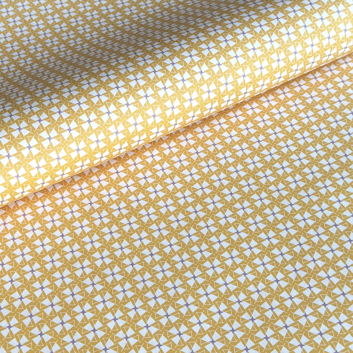 a sheet of wrapping paper with a geometric star pattern in white and purple on mustard yellow background