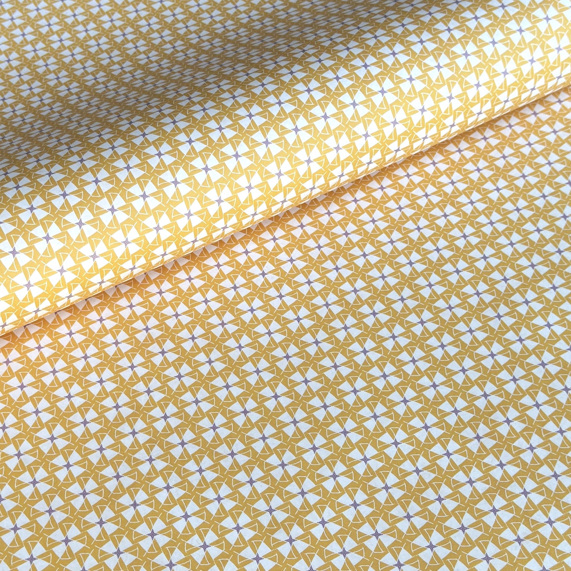 a sheet of wrapping paper with a geometric star pattern in white and purple on mustard yellow background