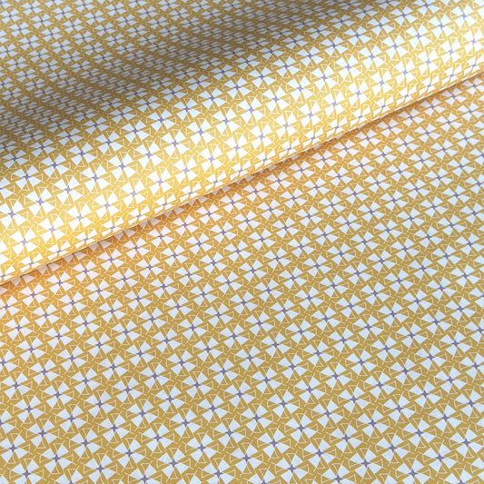 a sheet of wrapping paper with a geometric star pattern in white and purple on mustard yellow background