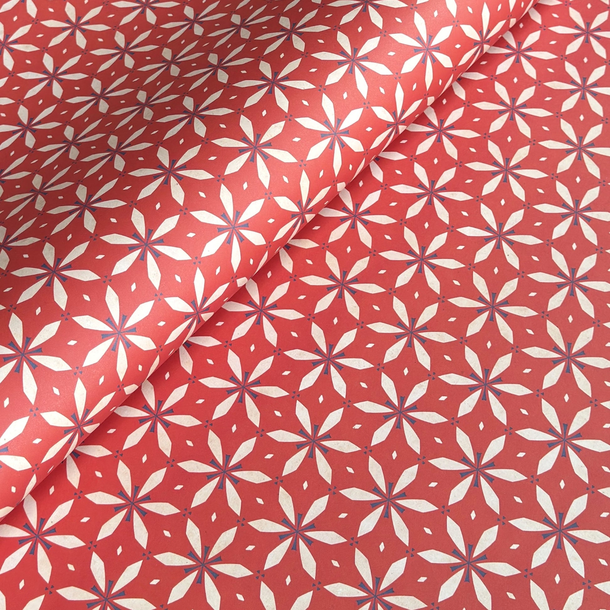 a sheet of wrapping paper with a floral geometric design in white and navy on red