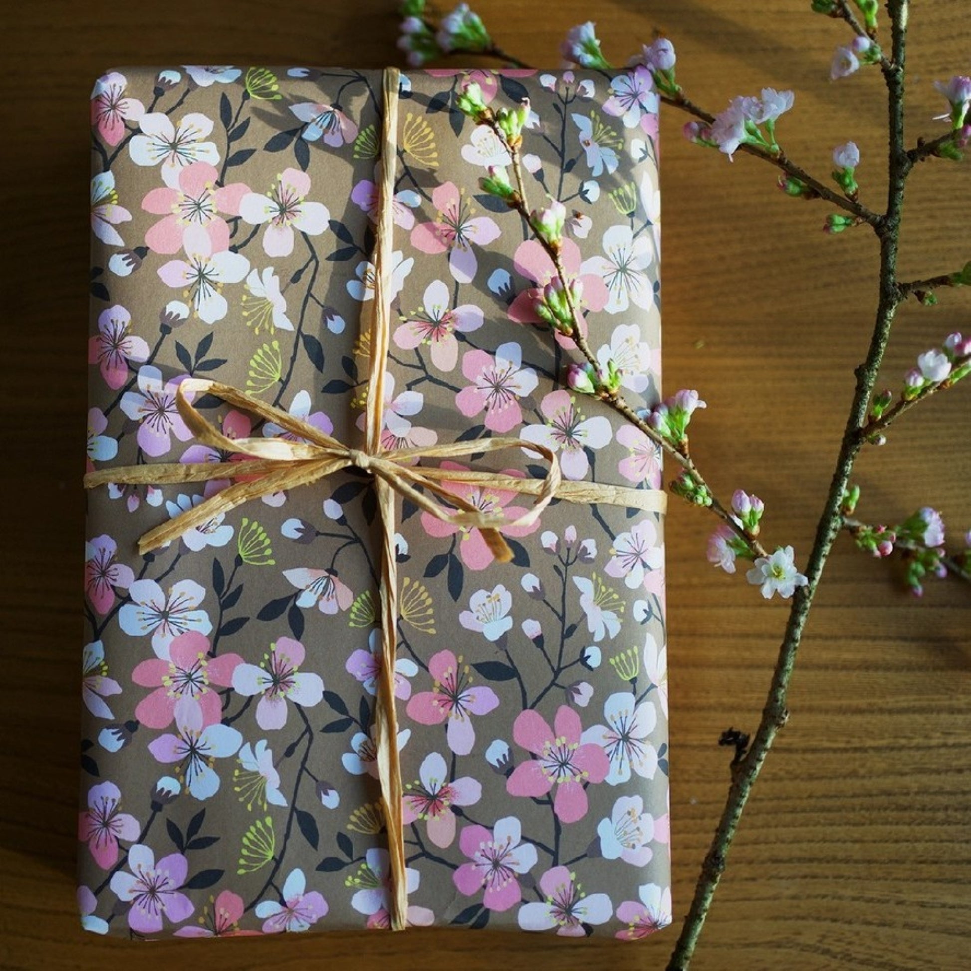 Cherry blossom patterned wrapping paper in pink, white and yellow on brown background