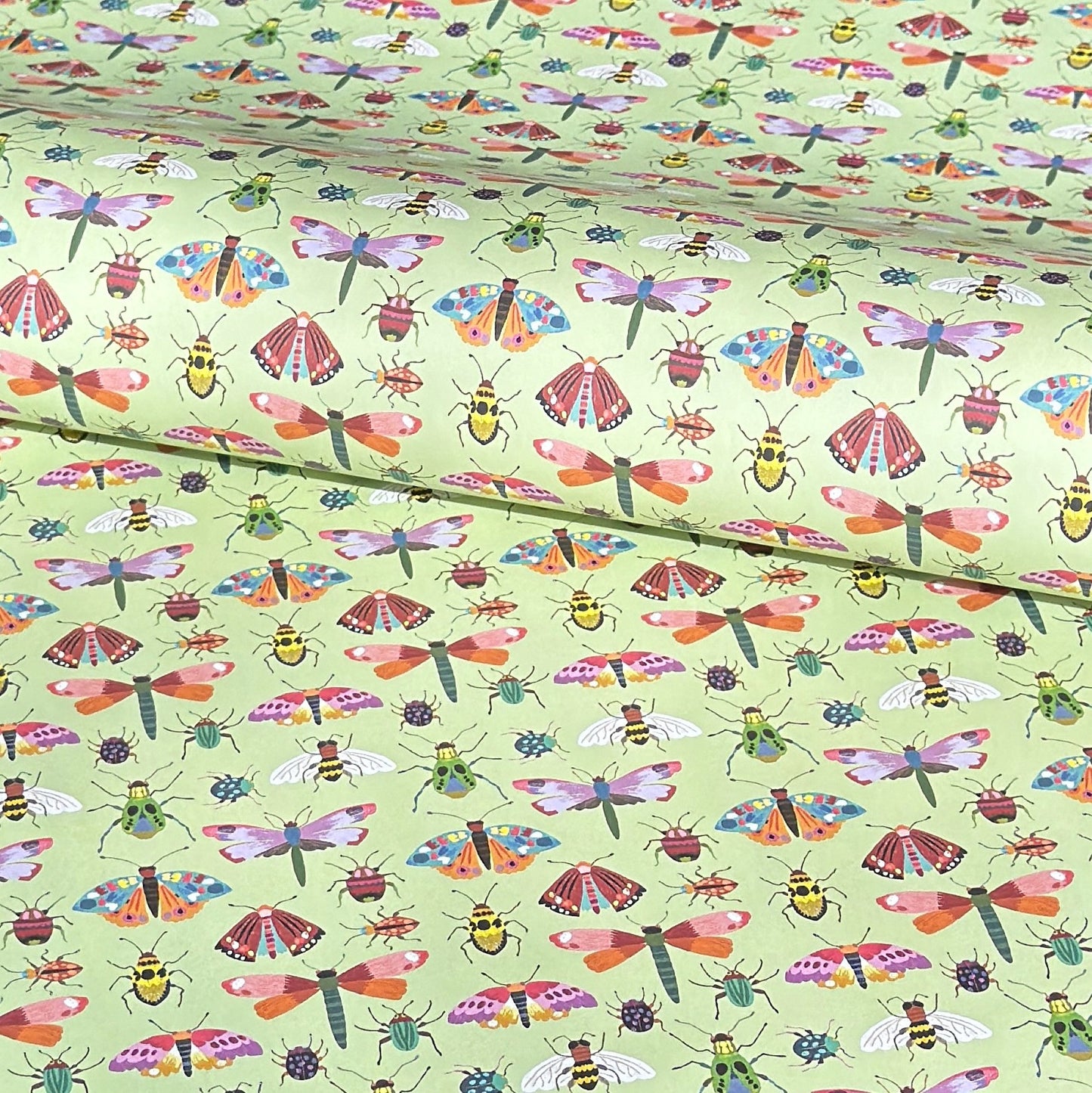 A sheet of wrapping paper with a pattern of colourful butterflies and insects on a light green background