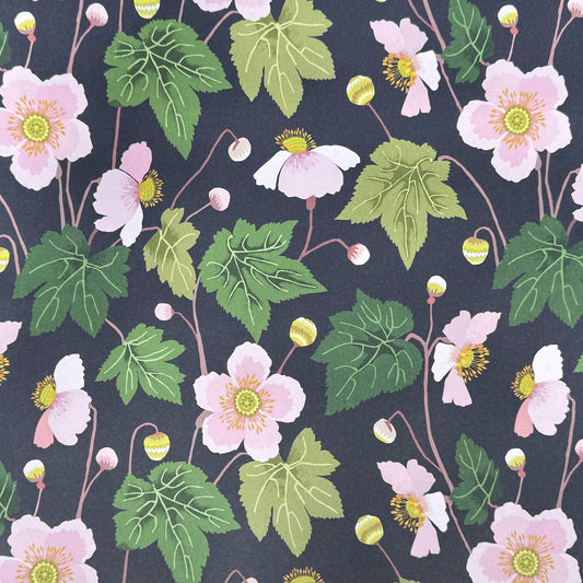 a sheet of wrapping paper with a dark indigo background and pink japanese anemone flowers and green foliage