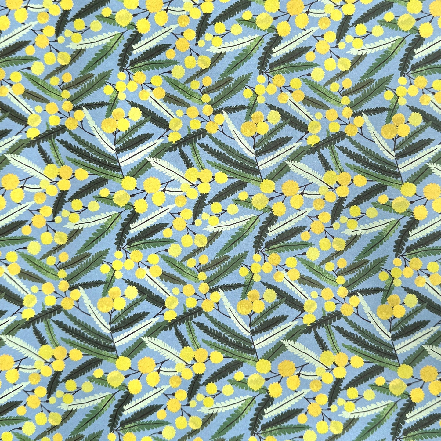 a sheet of wrapping paper with a pattern of yellow mimosa flowers and green leaves on a blue background