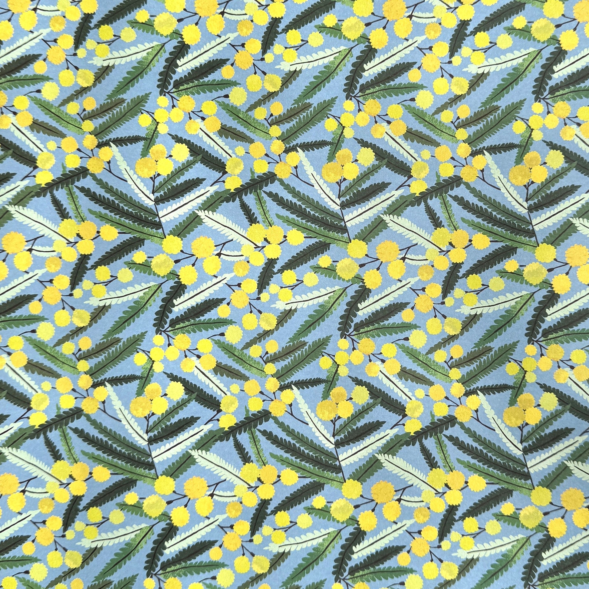 a sheet of wrapping paper with a pattern of yellow mimosa flowers and green leaves on a blue background