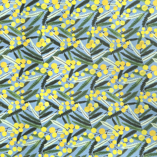 a sheet of wrapping paper with a pattern of yellow mimosa flowers and green leaves on a blue background