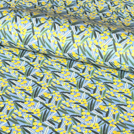 a sheet of wrapping paper with a pattern of yellow mimosa flowers and green leaves on a blue background