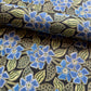 a sheet of wrapping paper with a stylised periwinkle flower design in blue and green on black, close up