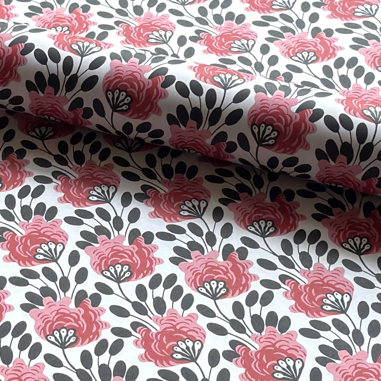 wrapping paper with a repeat design of pink flowers, black seedheads on white. Pictured rolled 