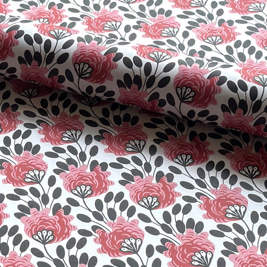 wrapping paper with a repeat design of pink flowers, black seedheads on white. Pictured rolled 