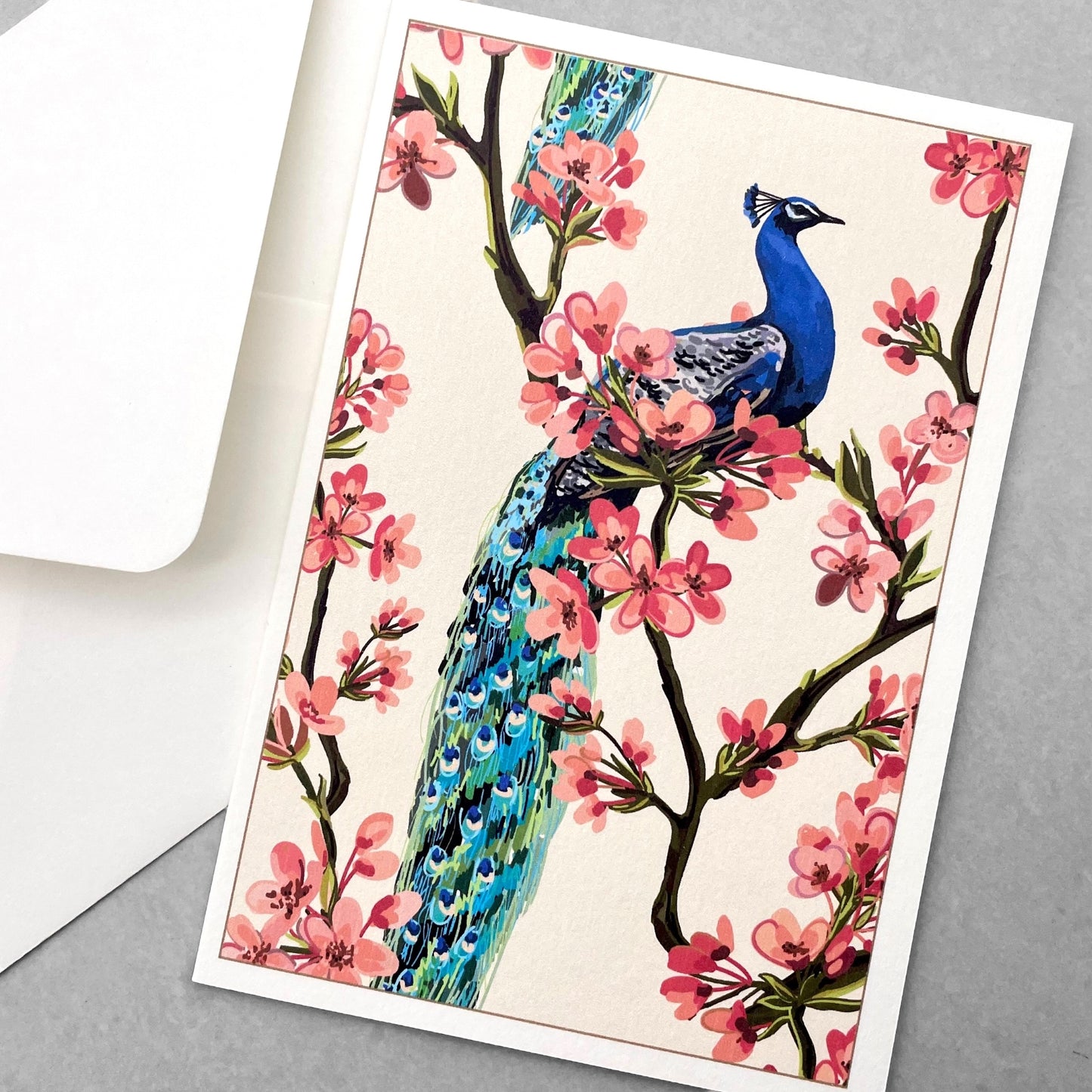 greetings card of a peacock on a branch of a tree in blossom by Com Bossa Studio