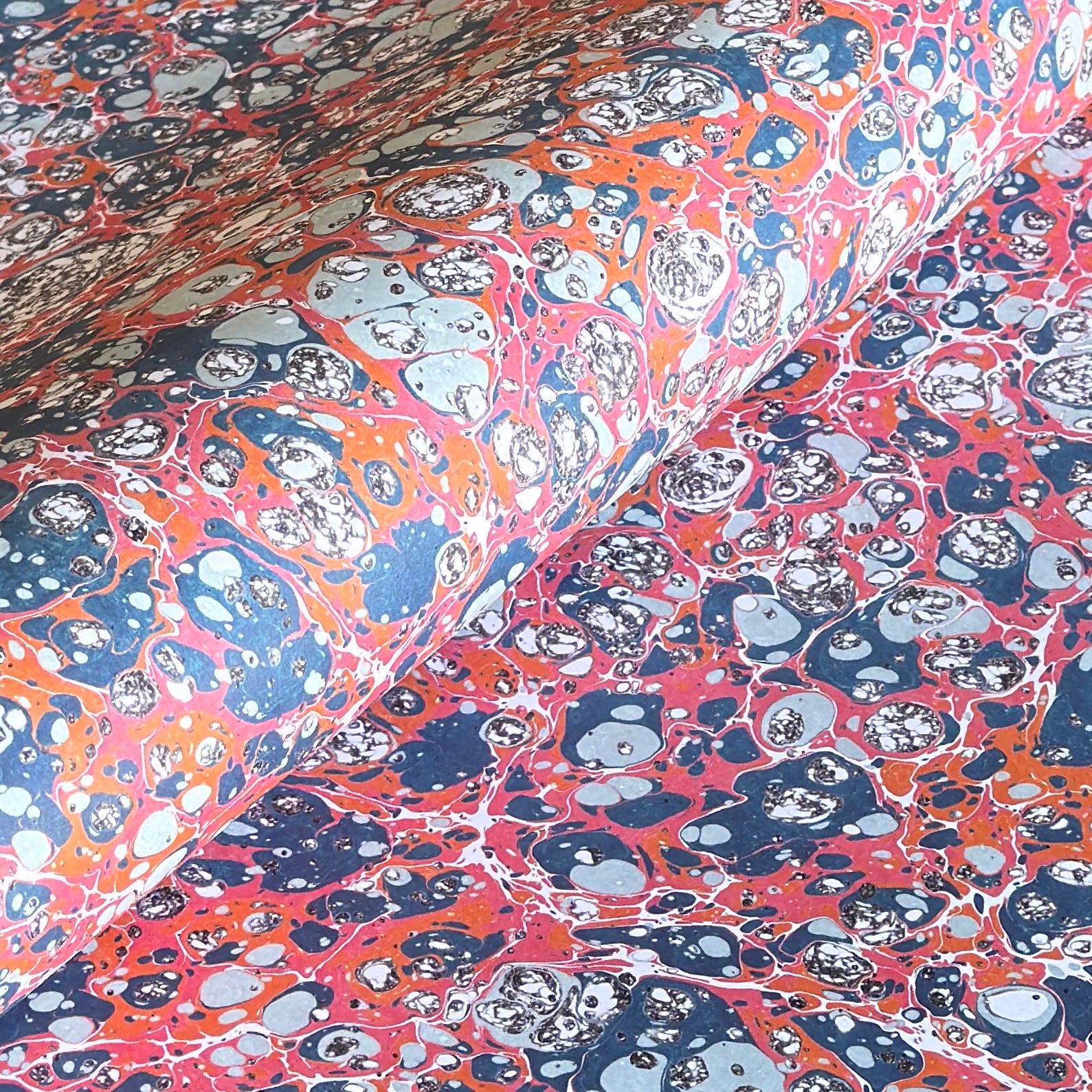 a printed marbled design wrapping paper in blue, orange and pink, by Compton Marbling