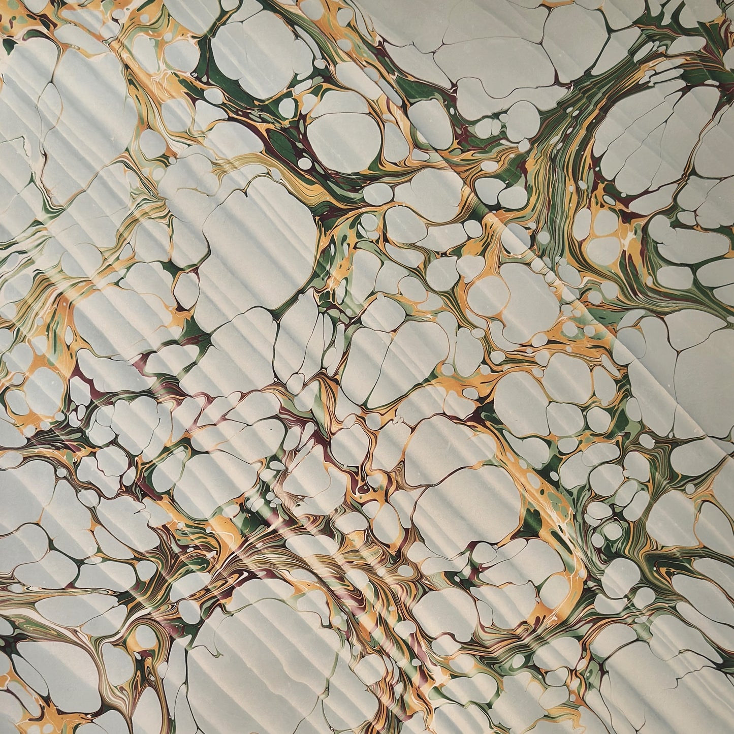 Printed marbled gift wrapping paper by Compton Marbling with a stone marbling pattern in soft grey, green and mustard.